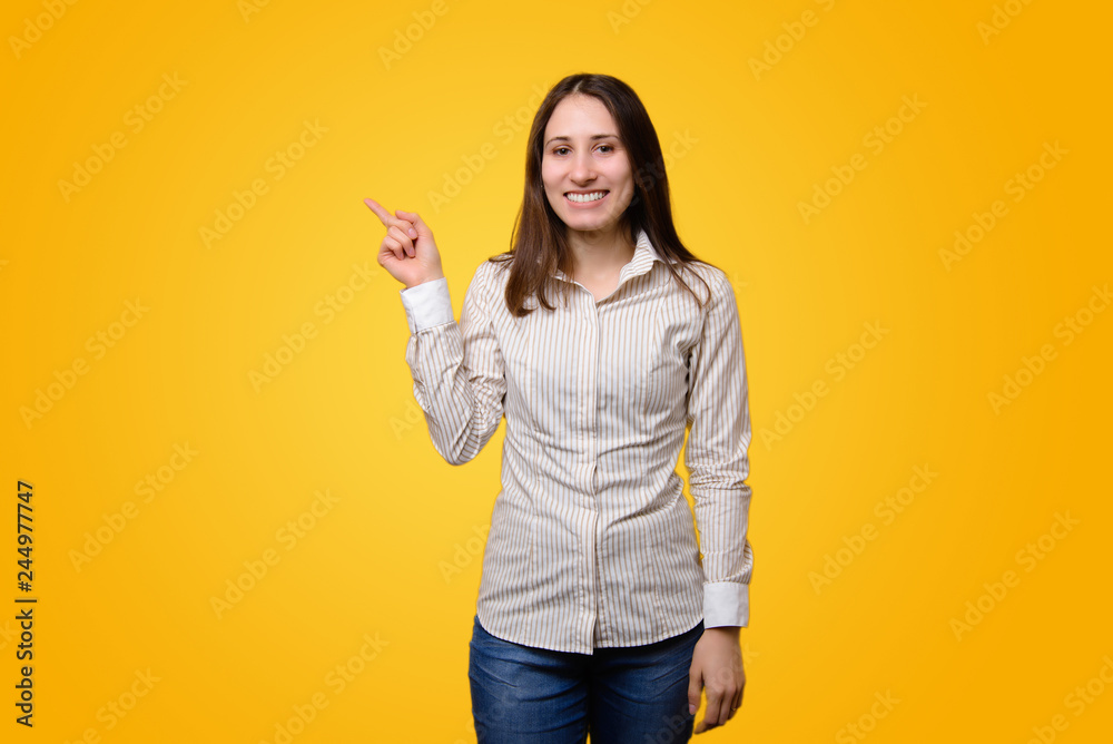 Smiling young woman in casual pointing away over yellow background