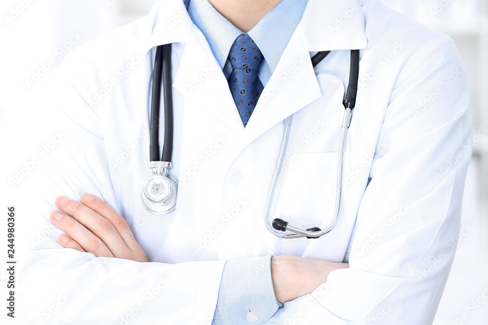 Male doctor standing upright with crossed arms, unknown physician at work. Medicine concept Male doctor standing upright with crossed arms, unknown physician at work. Medicine concept
