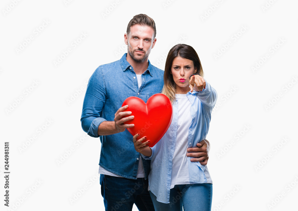 Young couple in love holding red heart over isolated background pointing with finger to the camera and to you, hand sign, positive and confident gesture from the front Young couple in love holding red heart over isolated background pointing with finger to the camera and to you, hand sign, positive and confident gesture from the front