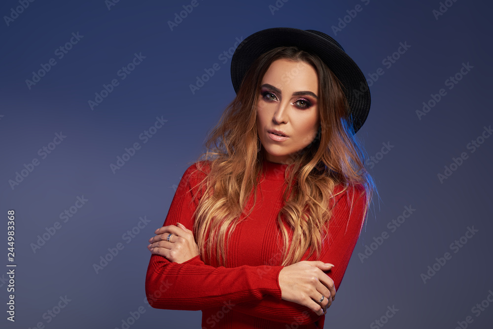 Portrait of wonderful white female model with bright makeup expressing energy on blue background. Lovely curly woman in stylish black hat Portrait of wonderful white female model with bright makeup expressing energy on blue background. Lovely curly woman in stylish black hat