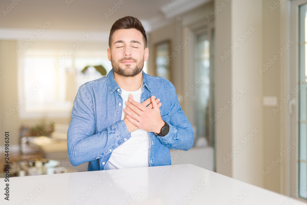 Young handsome man at home smiling with hands on chest with closed eyes and grateful gesture on face. Health concept.