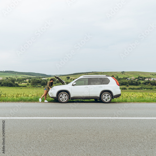 woman stand at roadside near broken car with opened hood