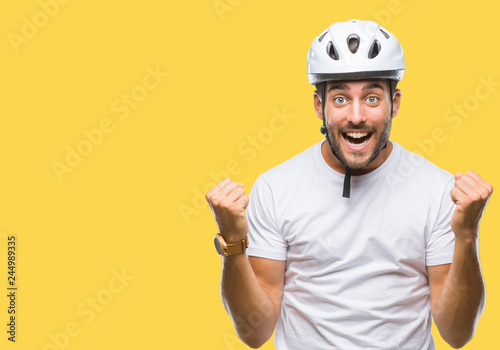 Fototapeta Young handsome man wearing cyclist safety helmet over isolated background celebrating surprised and amazed for success with arms raised and open eyes. Winner concept.