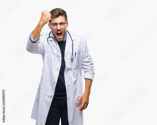 Young handsome doctor man over isolated background angry and mad raising fist frustrated and furious while shouting with anger. Rage and aggressive concept.