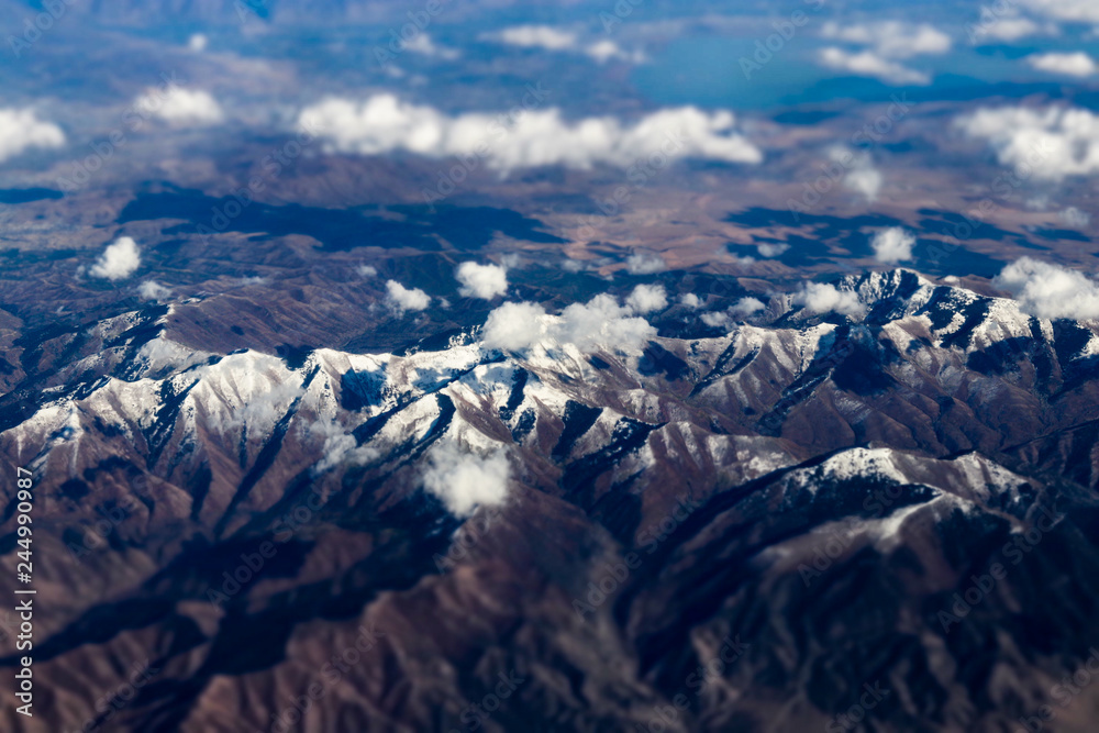 Fototapeta premium Aerial view of large snow capped mountains surrounded by dry desert
