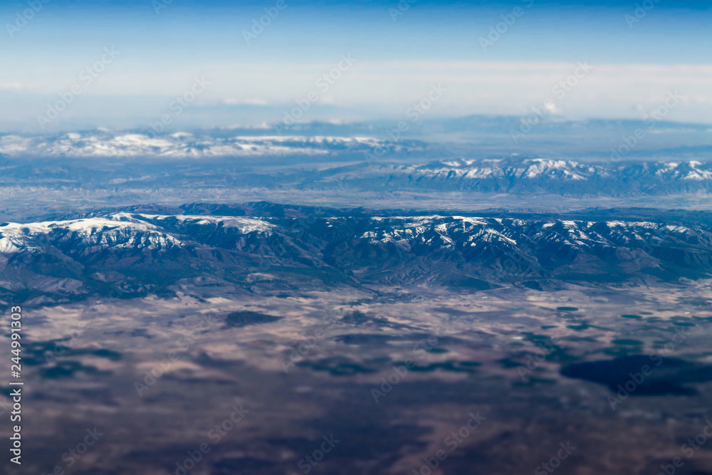 Aerial view of large snow capped mountains surrounded by dry desert