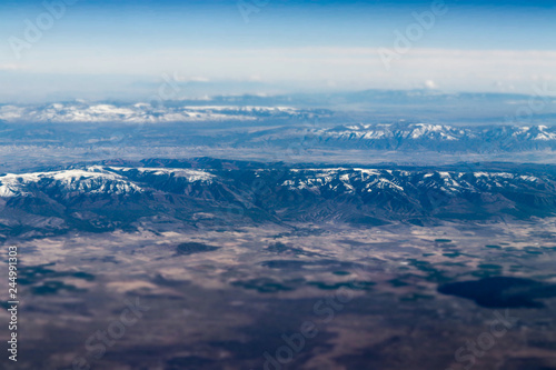 Aerial view of large snow capped mountains surrounded by dry desert © Nicholas