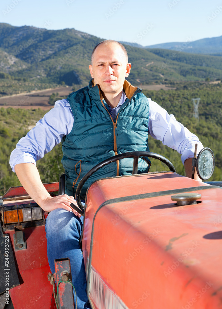 Confident  male owner of vineyard driving tractor outdoors in sunny day