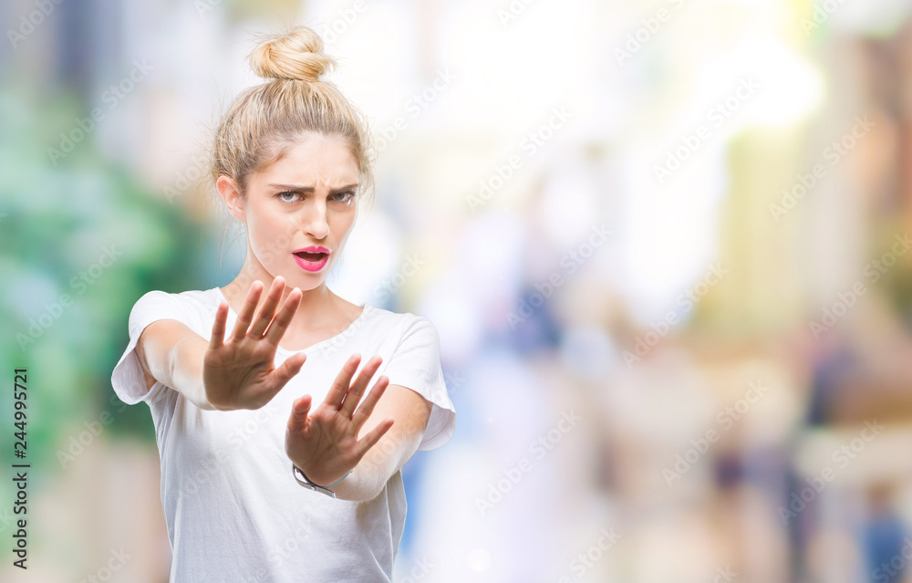 Young beautiful blonde woman wearing white t-shirt over isolated background afraid and terrified with fear expression stop gesture with hands, shouting in shock. Panic concept.