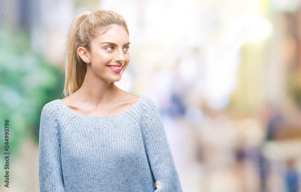 Young beautiful blonde and blue eyes woman wearing winter sweater over isolated background looking away to side with smile on face, natural expression. Laughing confident. Young beautiful blonde and blue eyes woman wearing winter sweater over isolated background looking away to side with smile on face, natural expression. Laughing confident.
