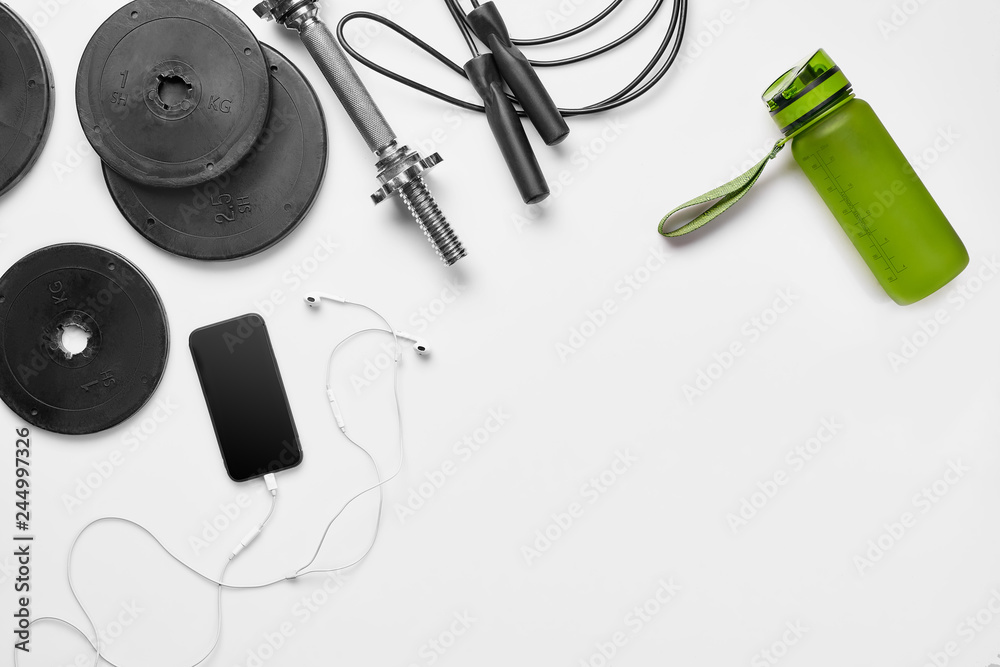 Fitness, healthy and active lifestyles concept, dumbbells, bottle of waters, smartphone with headphone, fitness bracelet on white background. Copy space for text. Top view
