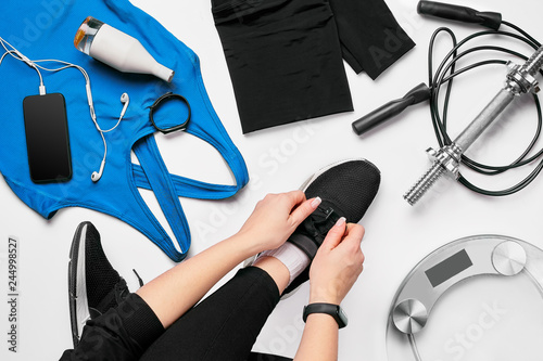 Young woman in sporting leggings laces sneakers, preparing for training. Accessories for sports on white background flat lay top view.