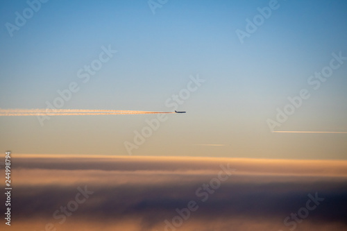 Condensation trails behind airplane in high altitude glowing in sunset