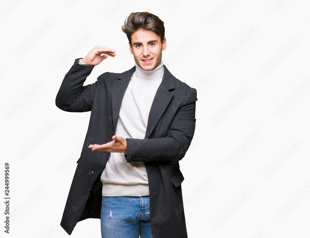 Young elegant man wearing winter coat over isolated background gesturing with hands showing big and large size sign, measure symbol. Smiling looking at the camera. Measuring concept. Young elegant man wearing winter coat over isolated background gesturing with hands showing big and large size sign, measure symbol. Smiling looking at the camera. Measuring concept.
