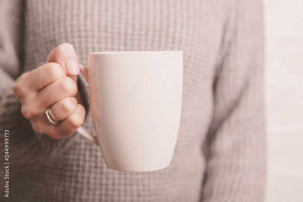 Female hand holding white cup in grey sweater background. Copy space Female hand holding white cup in grey sweater background. Copy space