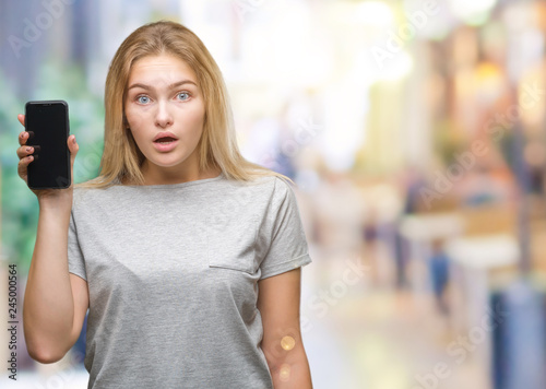 Young caucasian woman showing screen of smartphone over isolated background scared in shock with a surprise face, afraid and excited with fear expression
