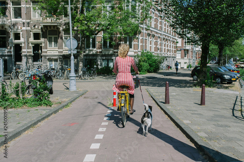 Photography Dutch woman walking her dog while riding the bicycle in Amsterdam, Netherlands