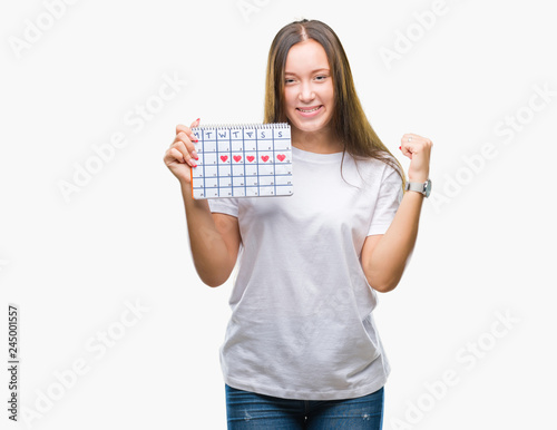 Young caucasian woman holding menstruation calendar over isolated background screaming proud and celebrating victory and success very excited, cheering emotion