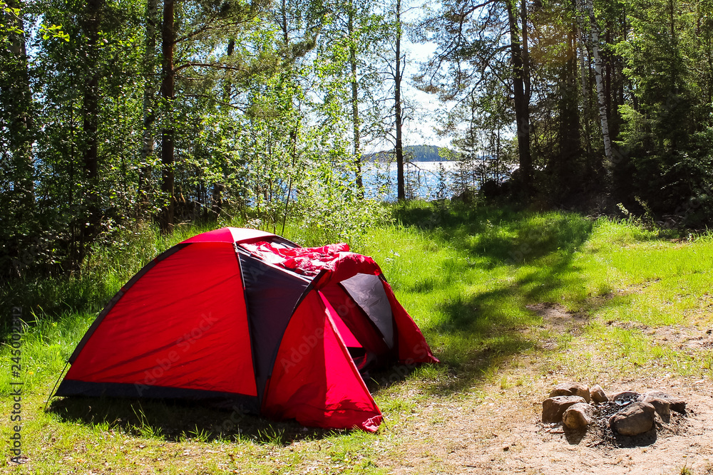 Camping in Finland (Scandinavia) with a red tent and fireplace in a forest near the lake during summer (Finland, Europe)