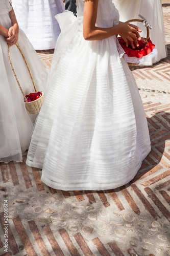 niñas llevando vestidos de comunión  blancos y largos con cesto con flores photo