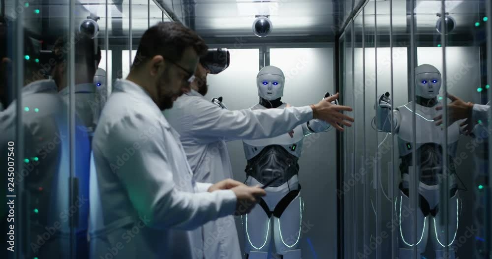 Medium shot of an engineer testing on robot controls using vr viewer while his colleague is holding a tablet Medium shot of an engineer testing on robot controls using vr viewer while his colleague is holding a tablet