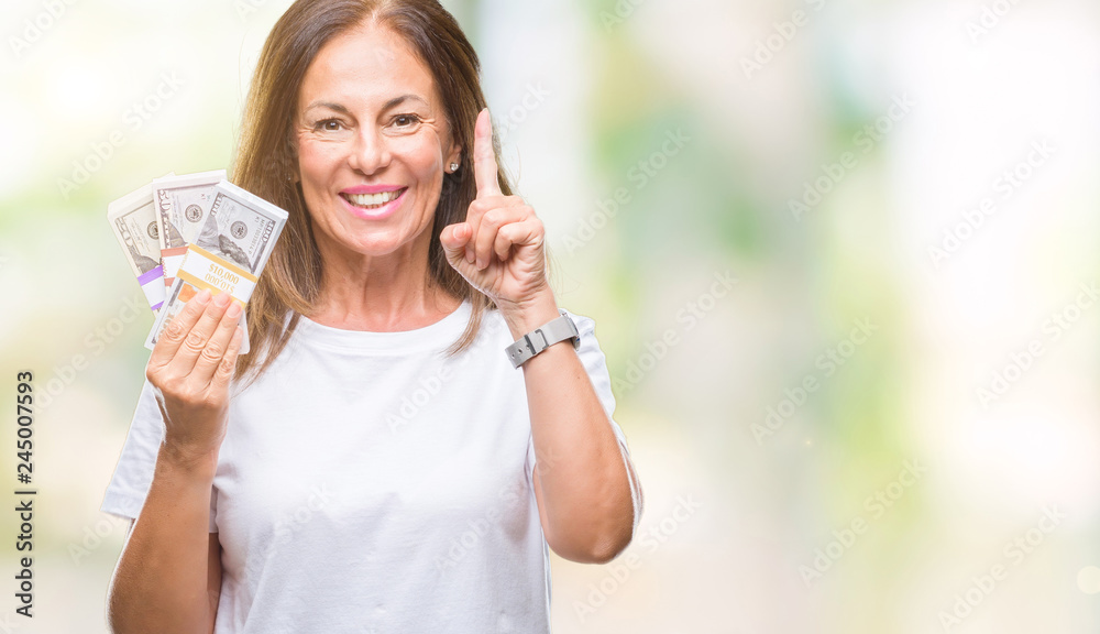 Middle age hispanic woman holding bunch of dollars over isolated background surprised with an idea or question pointing finger with happy face, number one
