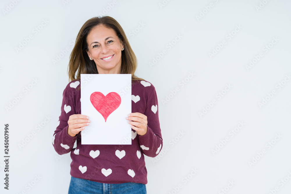 Middle age woman holding card gift with red heart over isolated background with a happy face standing and smiling with a confident smile showing teeth Middle age woman holding card gift with red heart over isolated background with a happy face standing and smiling with a confident smile showing teeth