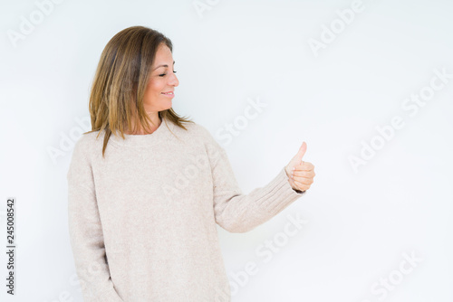 Beautiful middle age woman over isolated background Looking proud, smiling doing thumbs up gesture to the side