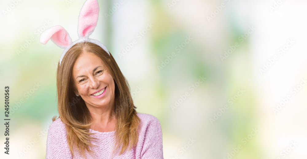 Middle age brunette woman wearing easter rabbit ears over isolated background happy face smiling with crossed arms looking at the camera. Positive person. Middle age brunette woman wearing easter rabbit ears over isolated background happy face smiling with crossed arms looking at the camera. Positive person.
