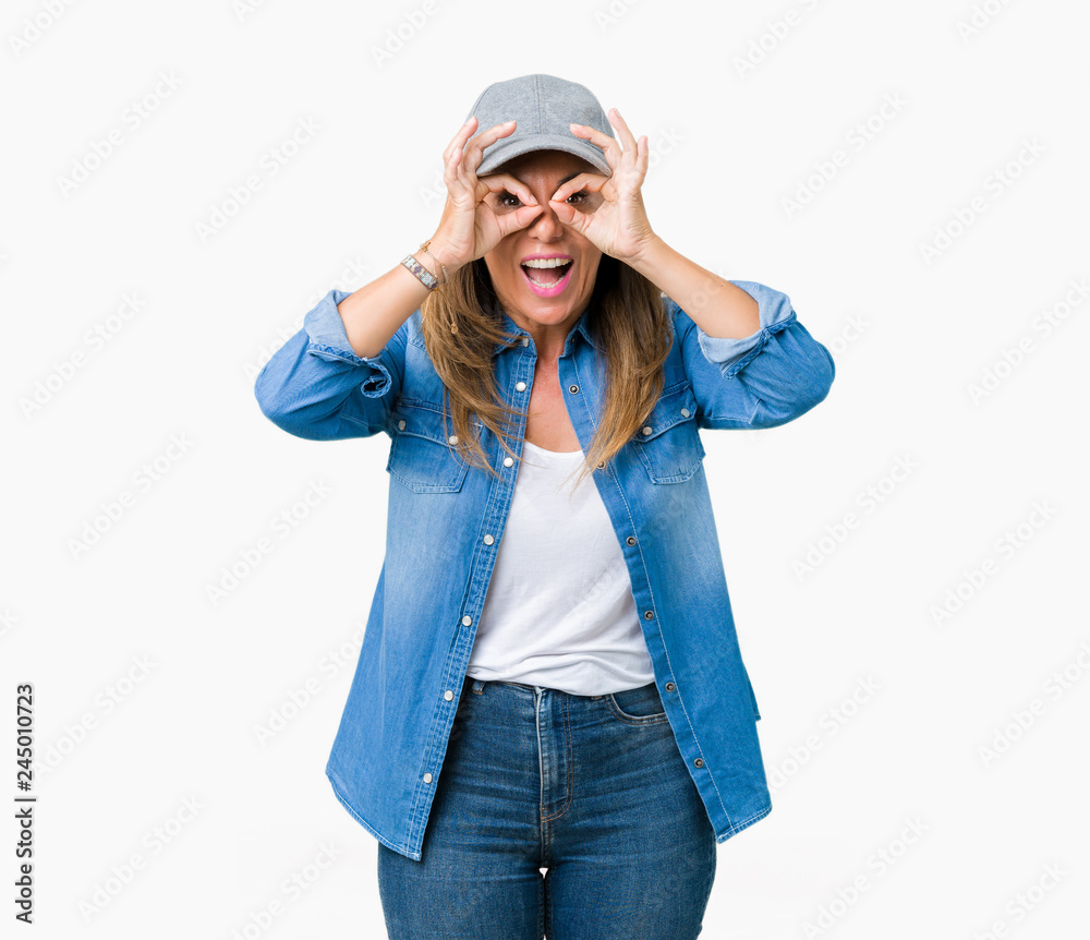 Beautiful middle age woman wearing sport cap over isolated background doing ok gesture like binoculars sticking tongue out, eyes looking through fingers. Crazy expression. Beautiful middle age woman wearing sport cap over isolated background doing ok gesture like binoculars sticking tongue out, eyes looking through fingers. Crazy expression.