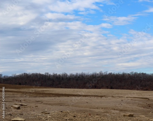 A dirt field with the forest and the clouds in the sky. 