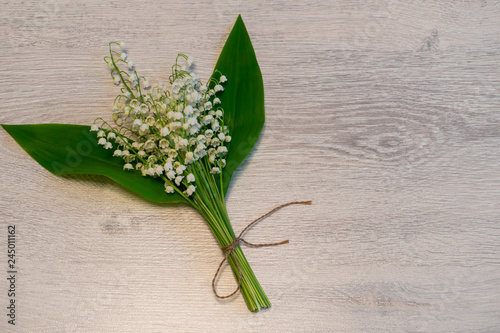 Bouquet of fresh lily of the valley flowers on light wooden background. Beautiful spring layout. Top view  copy space