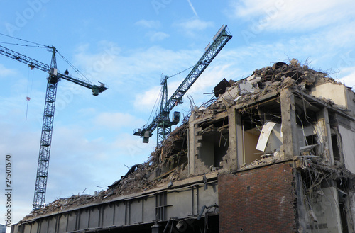 large cranes over a large concrete building being demolished with exposed walls during redevelopment of a large urban site
