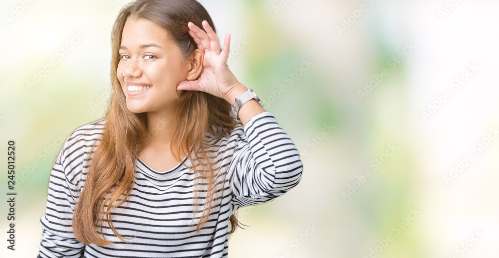 Young beautiful brunette woman wearing stripes sweater over isolated background smiling with hand over ear listening an hearing to rumor or gossip. Deafness concept. Young beautiful brunette woman wearing stripes sweater over isolated background smiling with hand over ear listening an hearing to rumor or gossip. Deafness concept.