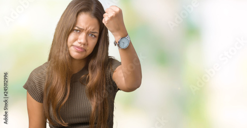 Young beautiful brunette woman over isolated background angry and mad raising fist frustrated and furious while shouting with anger. Rage and aggressive concept.