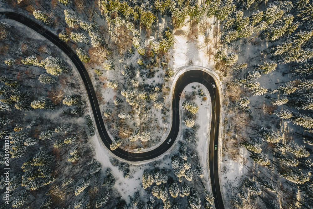 Traffic on a winter winding road in the middle of the forest aerial shot using a drone
