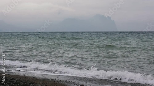 Storm surges of the sea washed the rocky beach with views of the mountains. Black Sea coast of Russia. Sea foam scatters to the winds. surf on the rocky coast