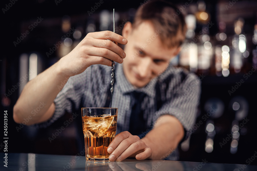 Barman prepares alcoholic cocktail in bar and with ice. Dark background