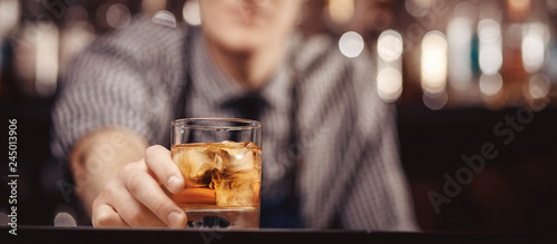 Fotografia Barman holds out glass of whiskey with ice to male visitor