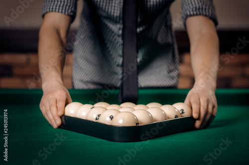 Male player puts white balls with triangle in Russian billiards on green table