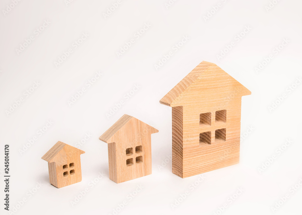 Three wooden houses stand in a row in order of increasing on a white background. The concept of buying and selling real estate. Residential area, rental and investment in real estate.