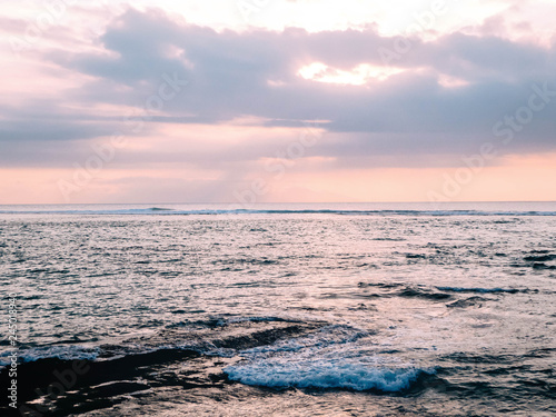 Sunset on Sengigi beach on the island of Lombok in Indonesia. Beautiful warm colored sunlight reflections on the water surface. In the distance Mount Agung can be seen, an active volcano on Bali.