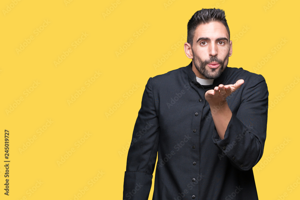 Young Christian priest over isolated background looking at the camera blowing a kiss with hand on air being lovely and sexy. Love expression. Young Christian priest over isolated background looking at the camera blowing a kiss with hand on air being lovely and sexy. Love expression.