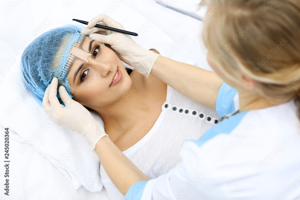 Professional beautician is going to correct eyebrow line at woman face using cosmetic ruler. Permanent brow makeup in beauty salon, closeup. Cosmetology treatment Professional beautician is going to correct eyebrow line at woman face using cosmetic ruler. Permanent brow makeup in beauty salon, closeup. Cosmetology treatment
