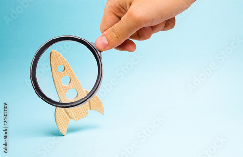 Magnifying glass is looking at the Rocket on a blue background. concept of a startup, education and the desire to research. Space tourism, flight to the moon or mars The rocket is ready to take off