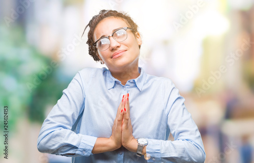 Young braided hair african american business girl wearing glasses over isolated background begging and praying with hands together with hope expression on face very emotional and worried
