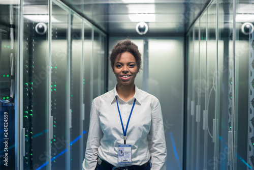 Adult IT worker in white shirt standing among server racks in data center smiling at camera