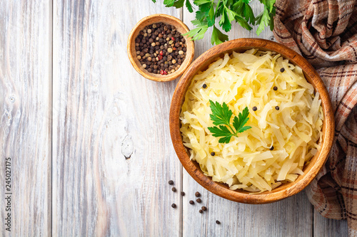 Homemade sauerkraut with black pepper and parsley in wooden bowl on rustic background. Top view. Copy space. photo