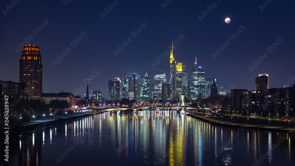 End of lunar eclipse of over the skyline of Frankfurt, Germany, with reflections on the river Main.