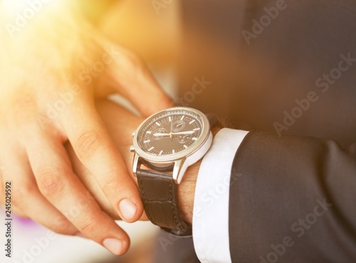 Businessman pointing at hand watch on grey wall background